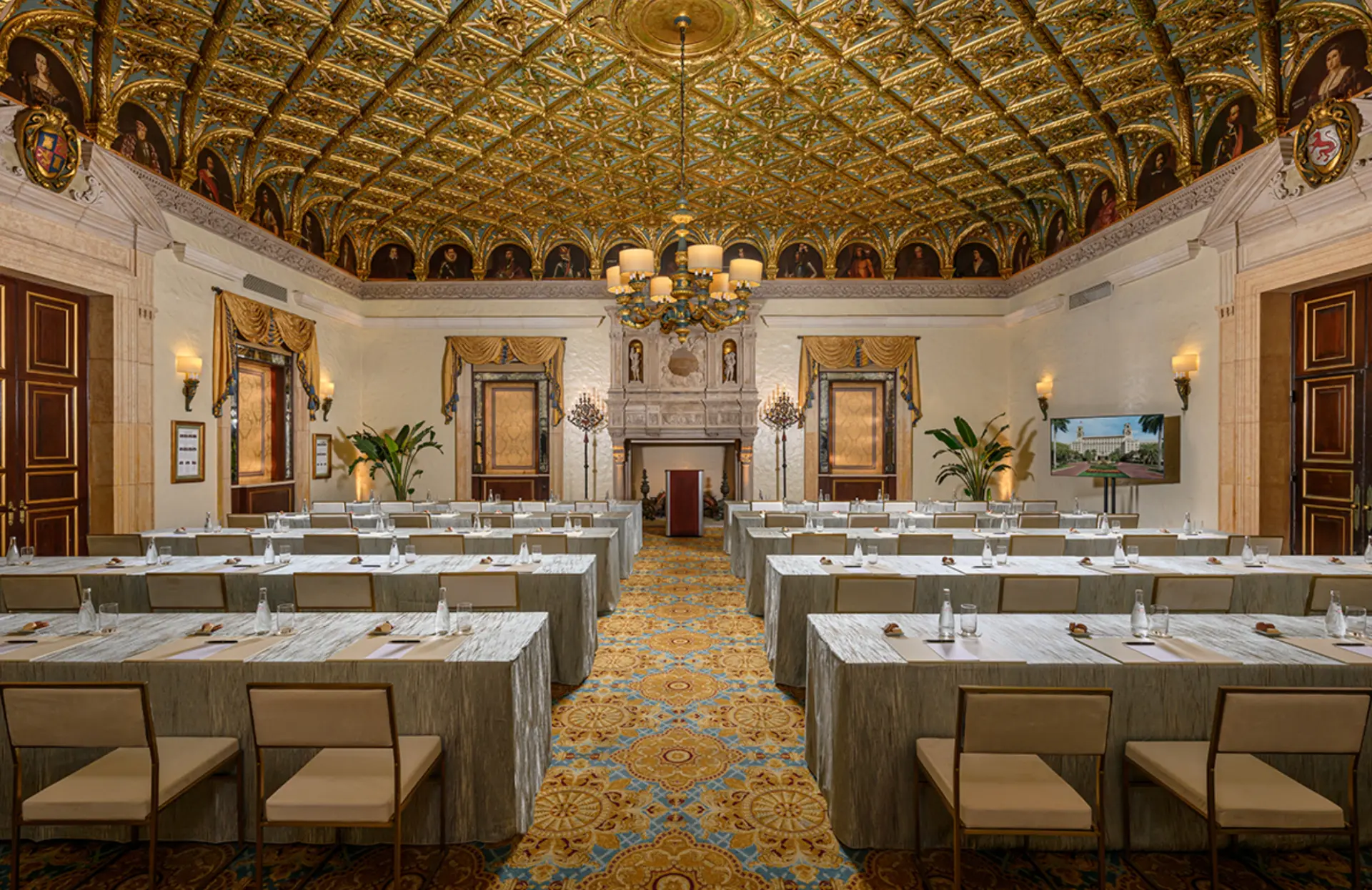 Gilded meeting room set with classroom-style tables beneath a gold coffered ceiling